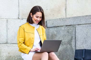 Dizüstü bilgisayar kullanan güzel Asyalı kadın. Merdivenlerde oturup dizüstü bilgisayar kullanan gülümseyen Asyalı kız. Dizüstü bilgisayar kullanan Asyalı iş kadını