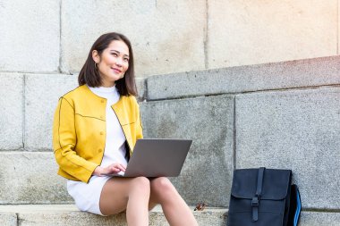 Dizüstü bilgisayar kullanan güzel Asyalı kadın. Merdivenlerde oturup dizüstü bilgisayar kullanan gülümseyen Asyalı kız. Dizüstü bilgisayar kullanan Asyalı iş kadını