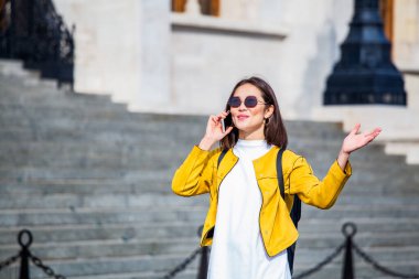 Güneşli bir yaz gününde sokakta yürüyen ve akıllı telefon kullanan Asyalı bir kadın. İş kadını cep telefonuyla konuşuyor.