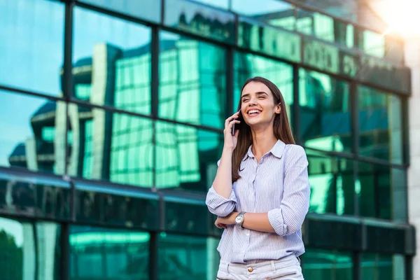 İşletme yöneticisi kadın arka planda ofis binalarıyla sokakta cep telefonuyla konuşuyor. Akıllı telefonlu genç bir kadın caddenin karşısında duruyor. Bina geçmişi bulanık..