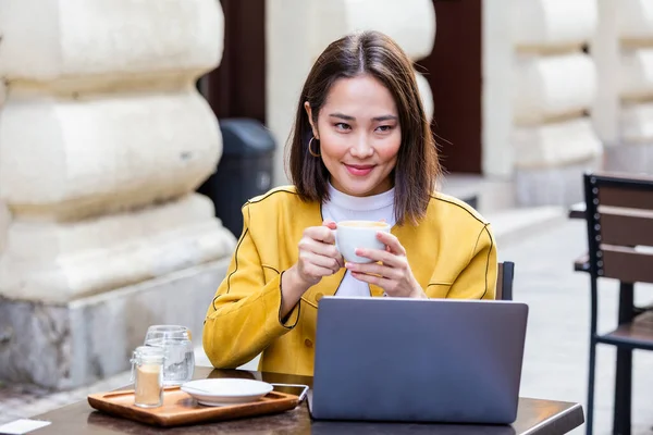 아시아의 여성은 커피숍에 탁자에 커피를 마시고 스마트폰을 합니다 노트북 있습니다 — 스톡 사진