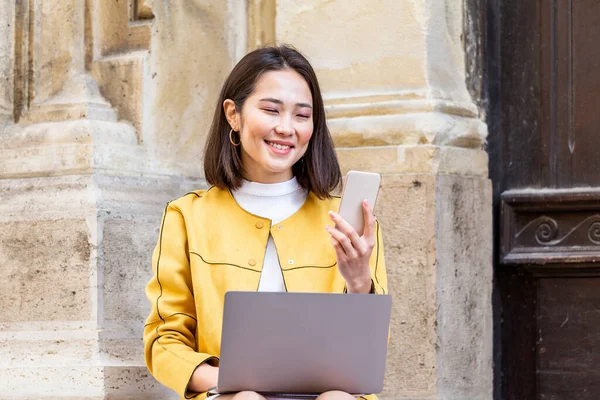 Dizüstü Bilgisayarda Çalışan Gülümseyen Asyalı Kadın Yerde Oturmuş Akıllı Telefonuyla — Stok fotoğraf