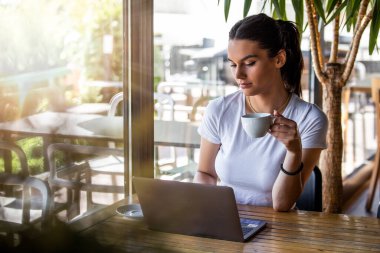 Pencerenin yanındaki kafede oturmuş kapuçino içen güzel bir kız. Kahve dükkanından dizüstü bilgisayarla çalışan güzel bir genç. Kafede dizüstü bilgisayarla oturan çekici bir kadın.