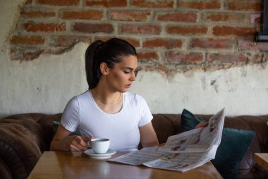 Kahvede dinlenirken güzel gülüşlü, gazete okuyan, boş zamanlarında kafede rahatlarken haber okuyan beyaz bir kadın.