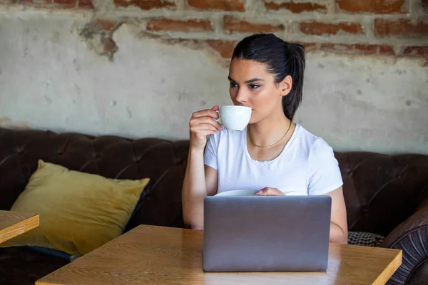 소파에서 휴식을 취하고 커피숍에서 노트북을 사용하고 여자가 커피를 마시고 있습니다 — 스톡 사진