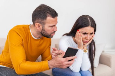 Boyfriend asking for an explanation to his cheater sad girlfriend sitting on a couch in the living room in a house interior