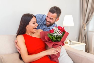 Sevecen genç adam sevgililer gününde sevgilisine sürpriz yapmak için güzel genç karısına bir buket kırmızı gül veriyor. Romantik mutlu çiftler Sevgililer Günü 'nde birlikte hediye paylaşıyorlar.