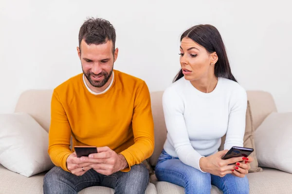 Jealous Young Woman Smartphone Looking Smiling Boyfriend Using Smartphone Home — Stockfoto