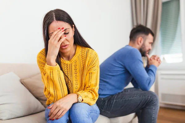 Married couple sitting together not looking at each other on couch in living room at home after quarrel. Angry husband frustrated wife. Break up, problems trouble in relationship concept
