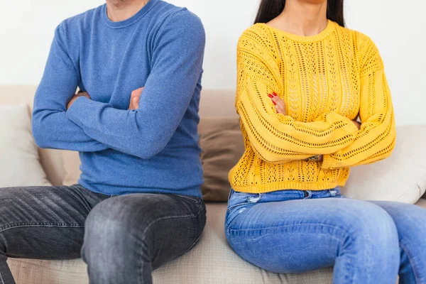 Young couple sitting back to back after a fight on the sofa. Young couple in fight with arms crossed sitting on couch after quarrel at home. Young woman and her boyfriend sitting next to each other angry