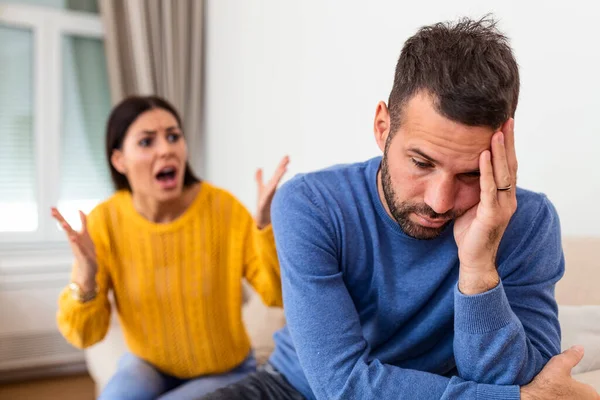 Angry young couple sit on couch in living room having family fight or quarrel suffer from misunderstanding, millennial husband and wife dispute involved in argument, relationships problems concept