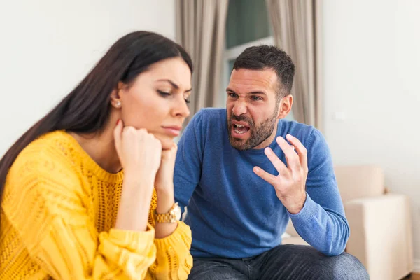 Young sad afraid woman and her violent screaming man. Young couple fighting at home, boyfriend shouting at girlfriend. Stressed out couple having problems. Divorce concept.