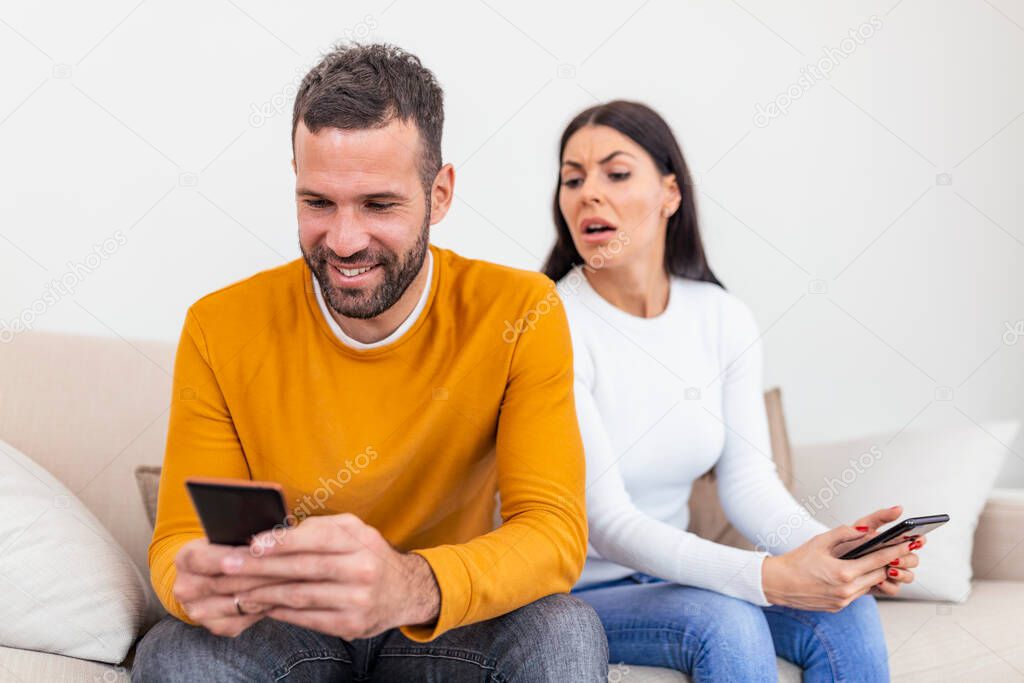 happy smiling man turned his back to wife, reading message on phone from his lover, worried woman sitting next to him, trying to peek at screen. Cheating and infidelity concept