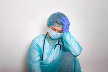 Coronavirus concept. COVID-19. Young female doctor in protective suit uniform, face mask and rubber gloves, before patient examination feeling exhausted and worried. Doctors are heroes.