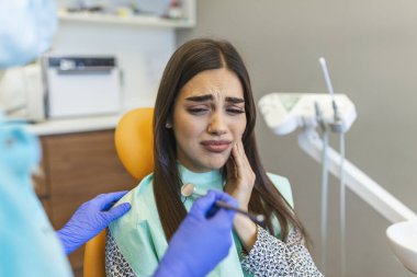 Dişçi koltuğunda oturan genç bir kadın, diş ağrısı çeken genç bir kadının diş hekimi koltuğunda otururken görüntüsü.