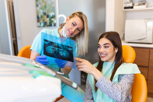 Female dentist explaining tooth x-rays to a patient. Dentist holding patient\'s orthopantogram