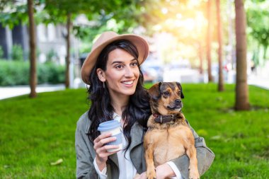 Beautiful young woman playing with her dogin a park outdoors. Lifestyle portrait. Cute young woman hugs her puppy dog. Love between owner and dog.