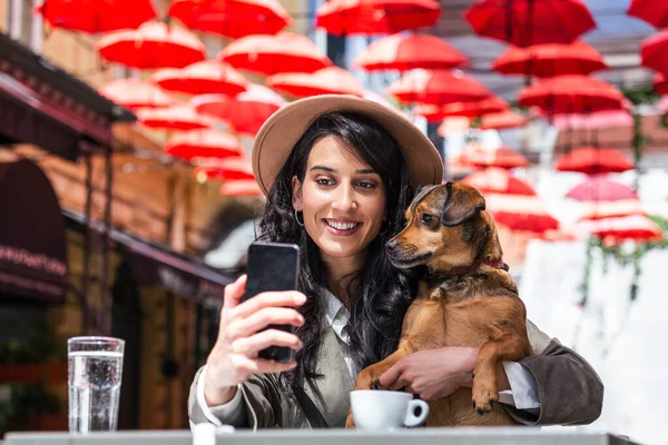 Young woman with her dog in pet friendly cafeteria. Girl drinking coffe at local coffee shop with her pet dog taking a selfie with mobile phone