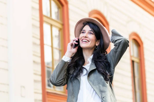 Young woman talking on mobile phone and looking away. Successful girl in casual calling on smartphone in city while standing on sidewalk. Beautiful woman talking on phone while walking on street.