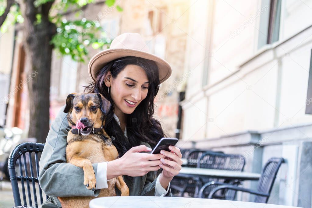 Young woman with her dog in pet friendly cafeteria. Young woman texting on her cell mobile phone while relaxing in cafe during free time with her dog