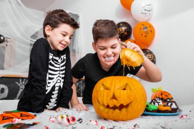 Kostümlü iki erkek kardeş masanın üstünde balkabağı olan Jack O 'Lantern' in içine bakıyor. Mutlu Cadılar Bayramı