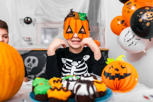 Cute little boy with pumpkin mask enjoying his halloween. Jack O' Lantern Halloween pumpkin on the table and other scary decorations