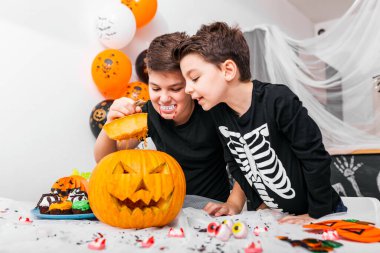 Kostümlü iki erkek kardeş masanın üstünde balkabağı olan Jack O 'Lantern' in içine bakıyor. Mutlu Cadılar Bayramı