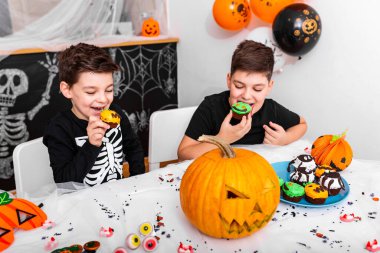 Cadılar bayramında eğlenen çocuklar etrafı korkunç dekorasyonlarla çevrili ve kek yemekten zevk alıyorlar. Jack O 'Lantern Cadılar Bayramı balkabağı ve çörekler masada. Mutlu Cadılar Bayramı!
