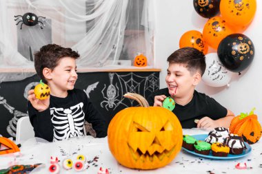 Mutlu Cadılar Bayramı! Kardeşiyle çekici bir çocuk Cadılar Bayramı partisine hazırlanıyor. Kostümlü kardeşler balkabağı ve keklerle eğleniyor..