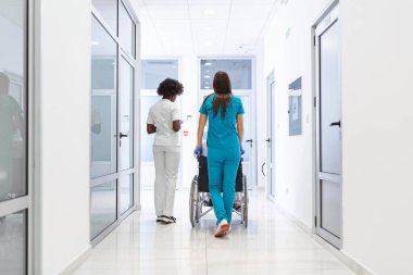 Wheelchair patient with professional African American female doctor and nurse specialist staff in corridor of hospital recovery center