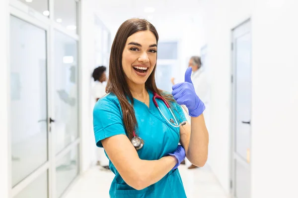 Portrait Smiling Female Doctor Wearing Scrubs Busy Hospital Corridor Showing — Φωτογραφία Αρχείου