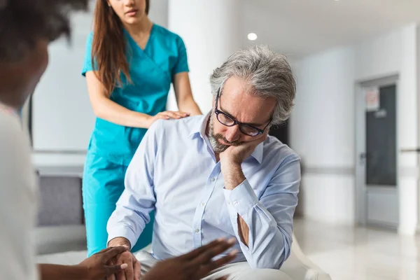 Caring young woman doctor comforting depressed unhealthy mature patient at meeting in hospital, therapist physician gp caregiver touching senior man shoulder, expressing empathy and support
