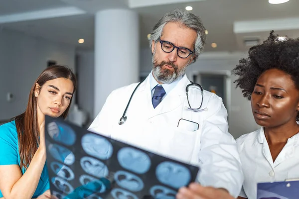 Experienced male Doctor helping his female colleagues with the interpretation of an X-ray of the lungs of a patient in the office