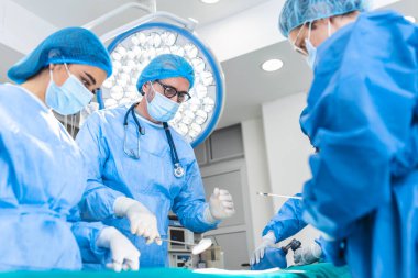 Team of doctors are standing in emergency room. Multi-ethnic surgeons are working at operating room at hospital. They are wearing blue scrubs.