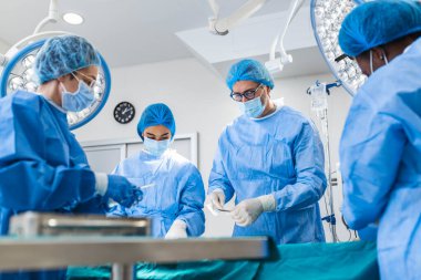 Multi-ethnic healthcare workers performing surgery on patient at operation theater. Medical colleagues operating in emergency room at hospital. They are in scrubs