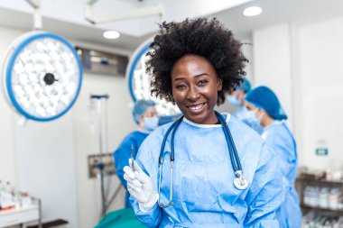 Portrait of smiling African American female surgeon in surgical uniform holding scalpel at operating room. Young woman doctor in hospital operation theater