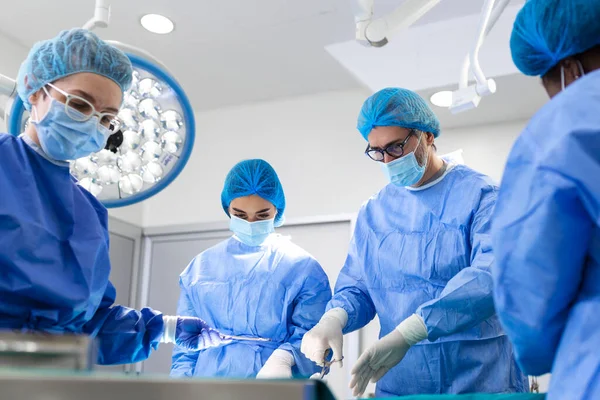 Portrait of team of multiethnic surgeons at work in a operation theatre. Several doctors surrounding patient on operation table during their work. Team surgeons at work in operating room.
