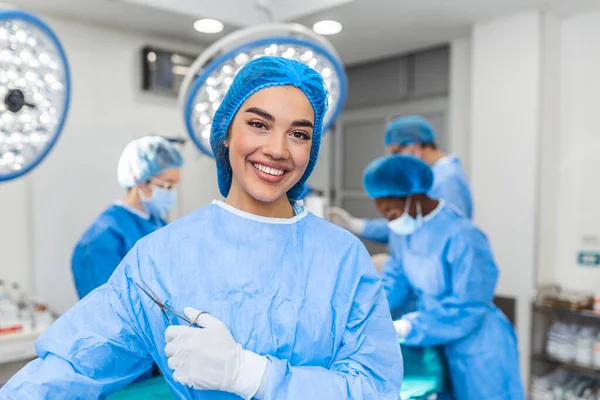 Portrait of female woman nurse surgeon OR staff member dressed in surgical scrubs gown mask and hair net in hospital operating room theater making eye contact smiling pleased happy looking at camera