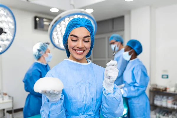 Plastic surgeon woman holding silicon breast implants in surgery room interior. Cosmetic surgery concept