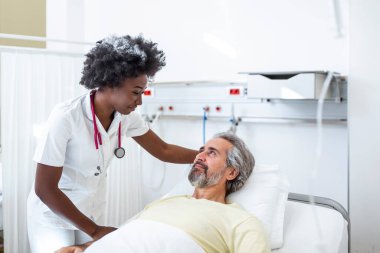 Yatakta yatan kıdemli hasta hastane odasında Afro-Amerikalı kadın doktorla konuşuyor. Sağlık ve sigorta konsepti. Doktor yaşlı hastayı hastane yatağında rahatlatıyor ya da sağlık danışmanlığı yapıyor..