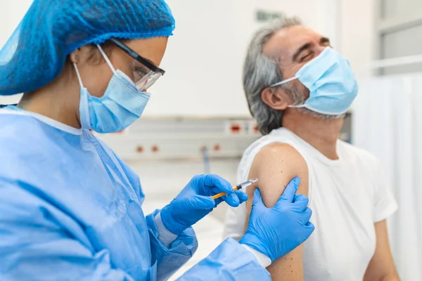 Vaccination, immunization, disease prevention concept. Man in medical face mask getting Covid-19 or flu vaccine at the hospital. Professional nurse or doctor giving antiviral injection to patient