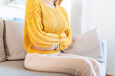 Evde yatarken karın ağrısı çeken genç bir kadın. Evde karın ağrısı çeken genç bir kadın. Jinekoloji konsepti. Evdeki kanepede acı çeken genç bir kadın.