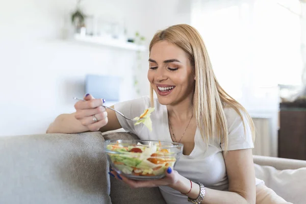 Healthy lifestyle woman eating salad smiling happy outdoors on beautiful day. Young female eating healthy food laughing and relaxing in sofa.