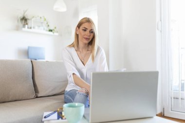 Defterde uzun saçlı güzel bir bayan evdeki kanepeye oturur - pazartesi siber satış için benzin dükkanlarını kontrol eder- alternatif ofis için teknoloji kadını konsepti