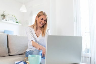 Olumlu genç kadın serbest yazar netbook 'ta video seyrediyor ve rahat bir evde kahve içiyor. Dizüstü bilgisayarda çalışan genç ve güzel bir iş kadını. İnternet 'e bağlanan serbest çalışan.