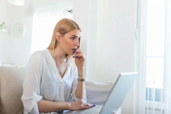 Nervous woman looking at laptop and biting her fingernails at home. Anxious depressed woman sitting with laptop and biting nails, looking nervous worried, scared of deadline stressful job.