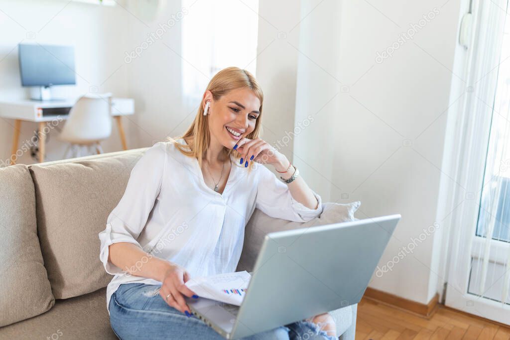 Smiling young woman using laptop at home, looking at screen, chatting, wearing wireless headset having video conference . business trainer tutoring by webcam, online training, e-coaching concept