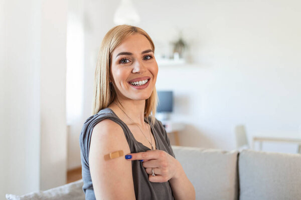 Woman pointing at his arm with a bandage after receiving the covid-19 vaccine. Young woman showing her shoulder after getting coronavirus vaccine
