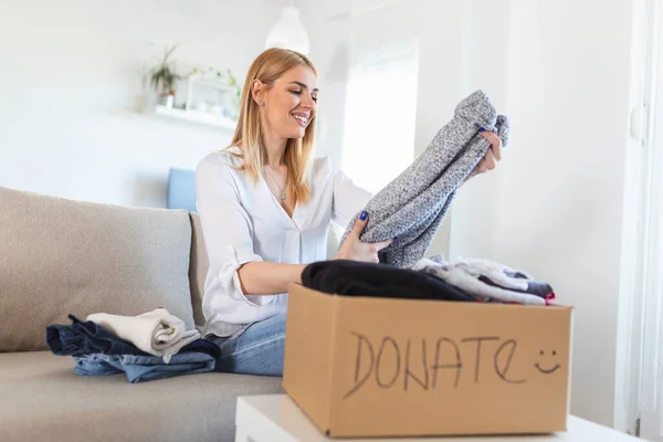 Donation Concept. Woman holding a Donate Box with full of Clothes. Woman holding a book and clothes donate box. Clothes in box for concept donation and reuse recycle