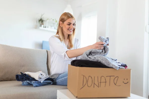 Happy Young Woman Sit Couch Stuck Clothes Donation Box Home — Stock fotografie